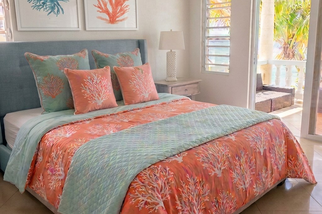 Master suite at Villa Amaaj with a king bed dressed in turquoise and coral accent pillows, a quilted throw, and doors to a sea-view balcony